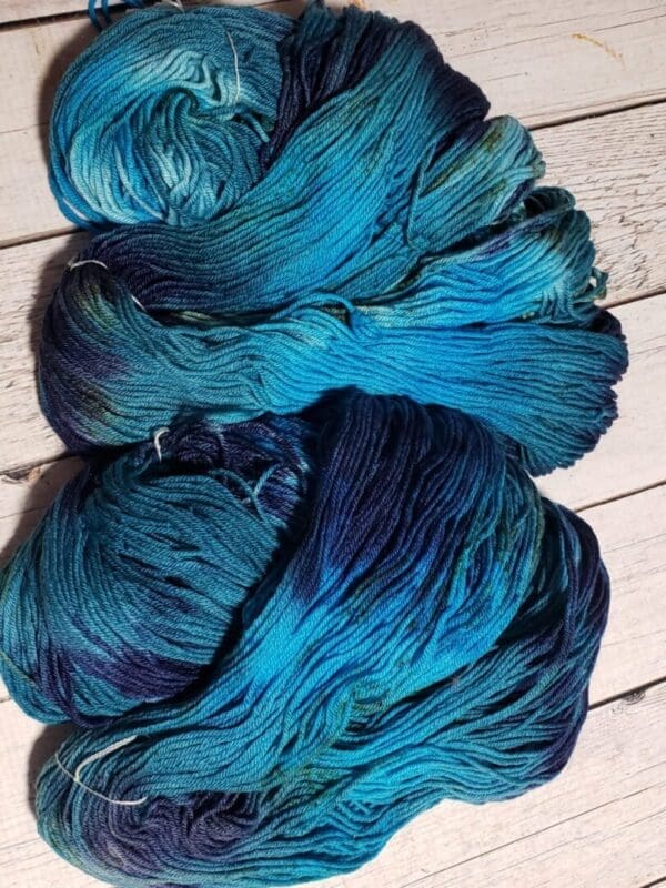 A skein of Mariana ~ Lotus Shaniko™ Luxury Fingering yarn on a wooden floor.