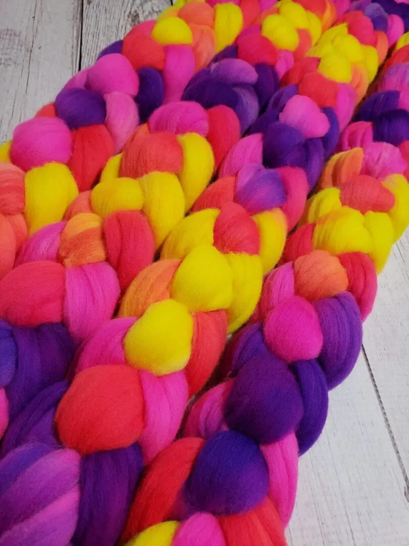 A bunch of Disco Date ~ 100g Hand-Dyed Luxury Combed Top Fiber laying on top of a wooden table.