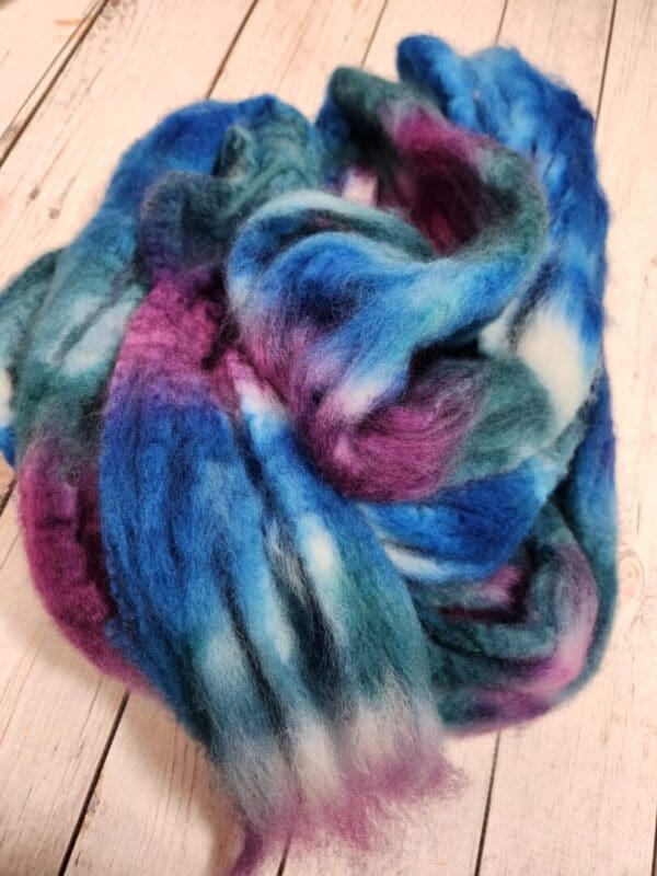 A pile of Disco Date ~ 100g Hand-Dyed Luxury Combed Top Fiber on a wooden floor.