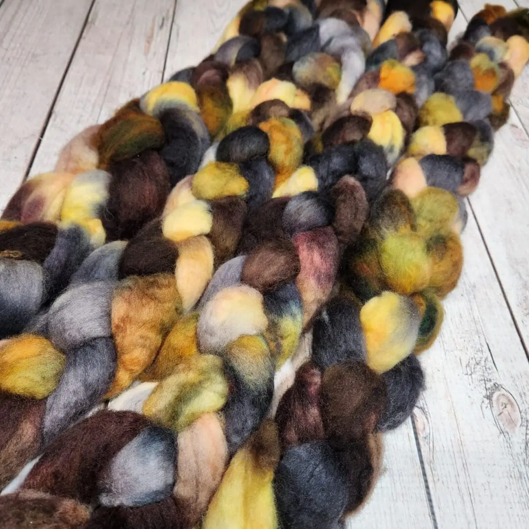 A bunch of Disco Date ~ 100g Hand-Dyed Luxury Combed Top Fibers on a wooden table.