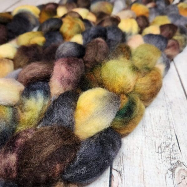 A bunch of Disco Date ~ 100g Hand-Dyed Luxury Combed Top Fiber on top of a wooden table.