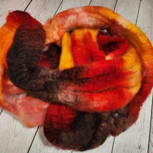 A red, orange, yellow, and brown Disco Date ~ 100g Hand-Dyed Luxury Combed Top Fiber skein on a wooden floor.