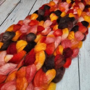 A bunch of Disco Date ~ 100g Hand-Dyed Luxury Combed Top Fiber, in red, orange and yellow, laying on a wooden floor.