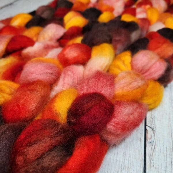 A pile of Disco Date ~ 100g Hand-Dyed Luxury Combed Top Fiber on a wooden table.