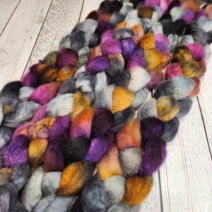 A skein of Disco Date ~ 100g Hand-Dyed Luxury Combed Top Fiber, purple, gray, and black roving.