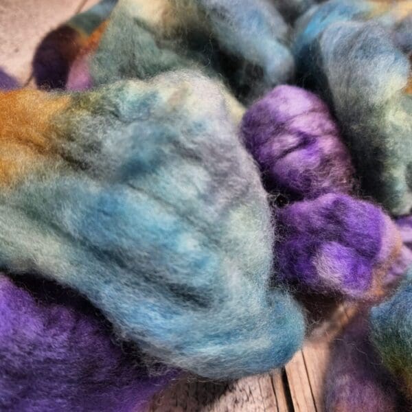 A pile of Disco Date ~ 100g Hand-Dyed Luxury Combed Top Fiber in purple, blue, and green.