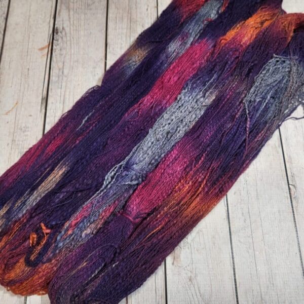 A skein of purple and orange yarn on a wooden floor.