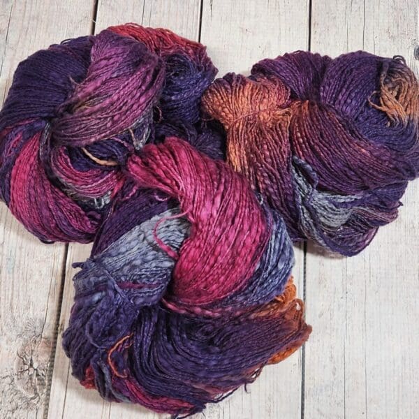 Three skeins of purple and orange yarn on a wooden table.