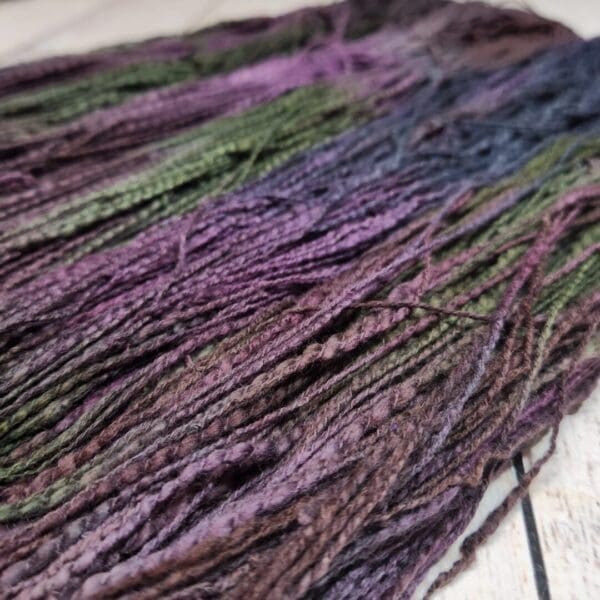 A skein of purple and green yarn on a wooden table.