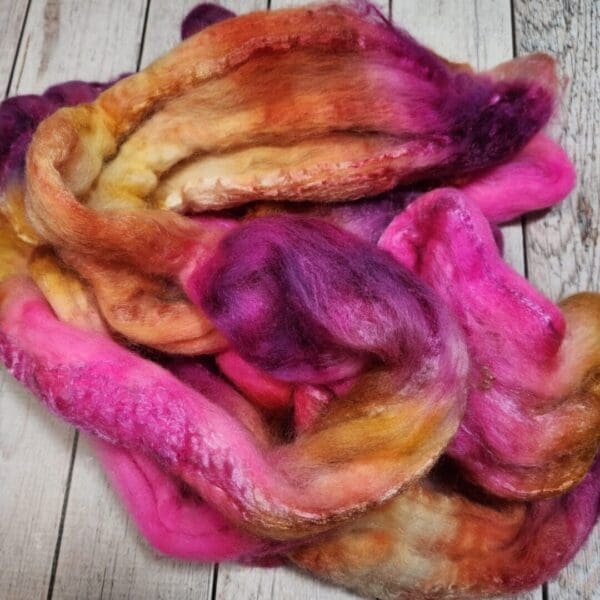 A pile of purple, pink, and orange Disco Date ~ 100g Hand-Dyed Luxury Combed Top Fiber on a wooden surface.