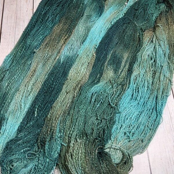 Two skeins of green and blue yarn on a wooden table.