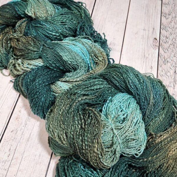 A skein of green and blue yarn on a wooden floor.