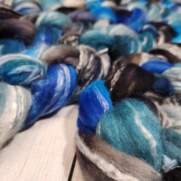 A skein of blue and black roving on a wooden table.