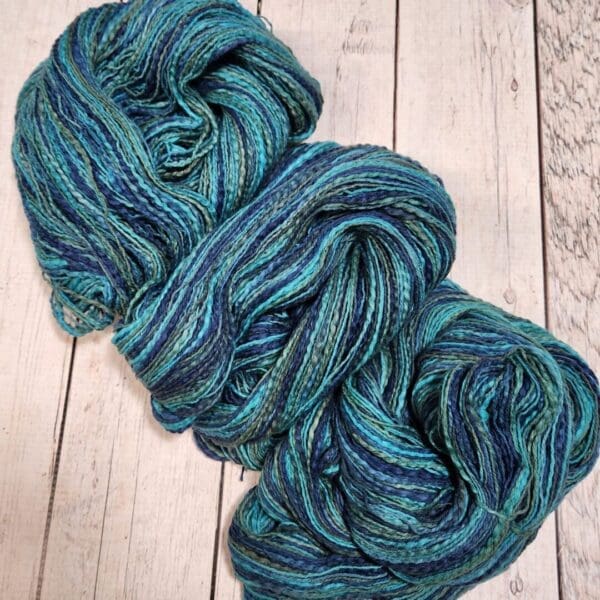 Two skeins of blue and green yarn on a wooden surface.