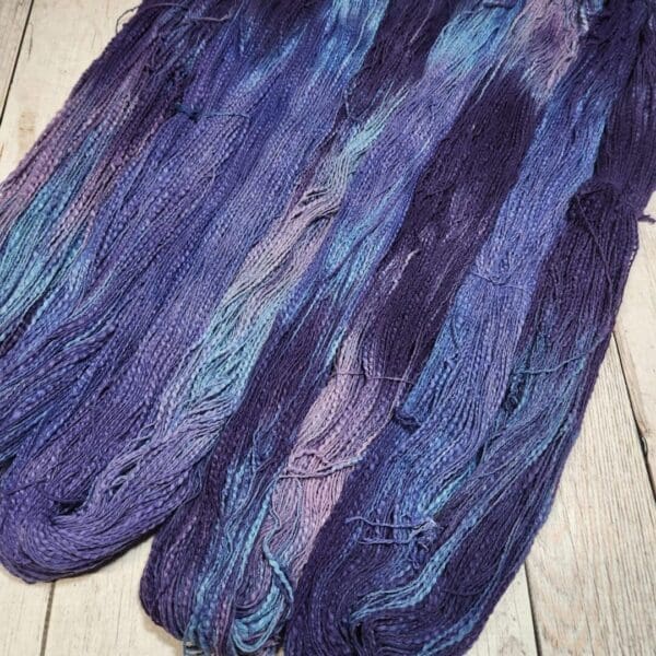 A skein of purple and blue yarn on a wooden floor.