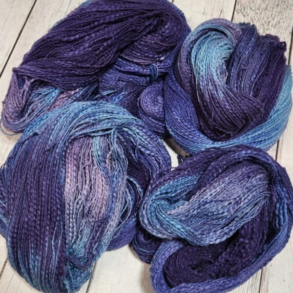 Three skeins of blue and purple yarn on a wooden table.