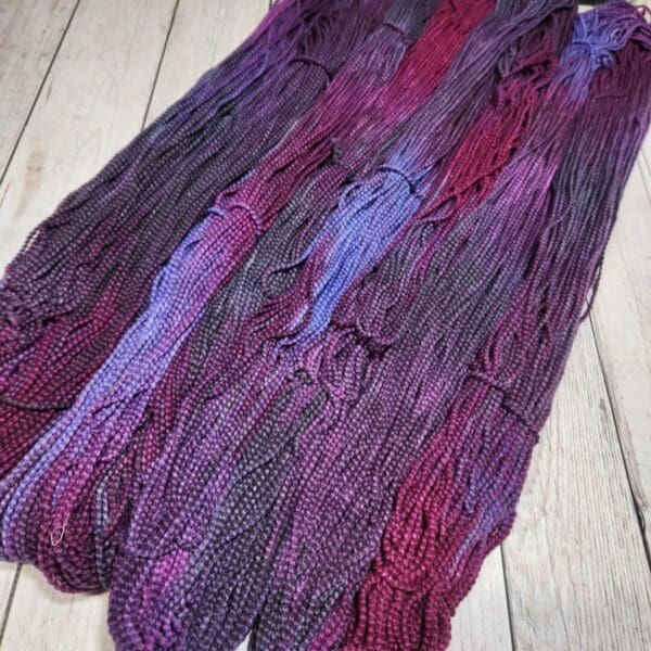 Purple and blue skeins of yarn on a wooden floor.