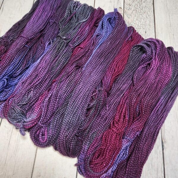 Skeins of purple and blue yarn on a wooden floor.