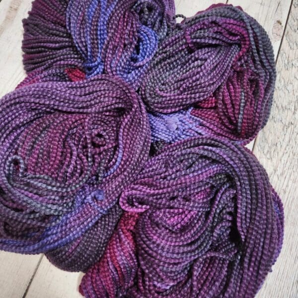 Skeins of purple and blue yarn on a wooden floor.