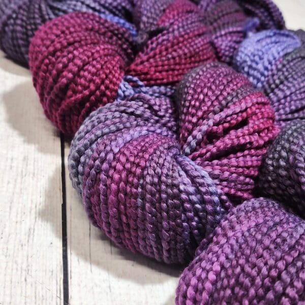 Purple and grey yarn laying on a wooden table.