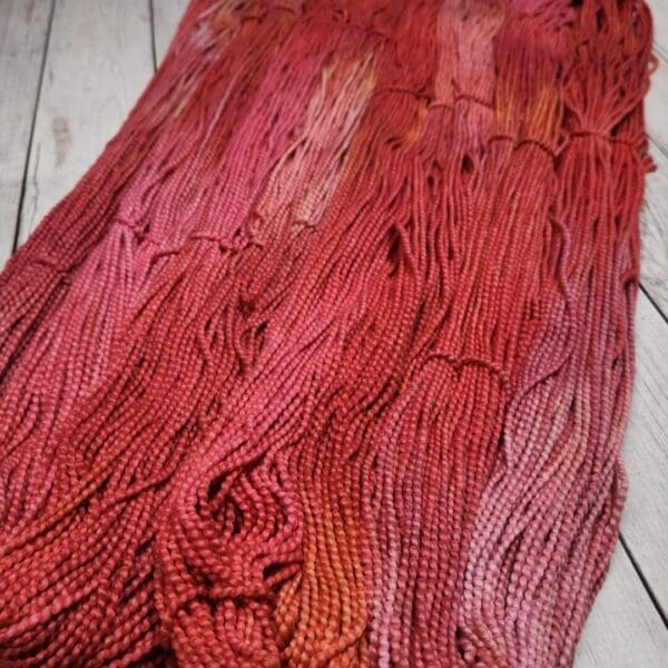 A skein of red and orange yarn on a wooden floor.