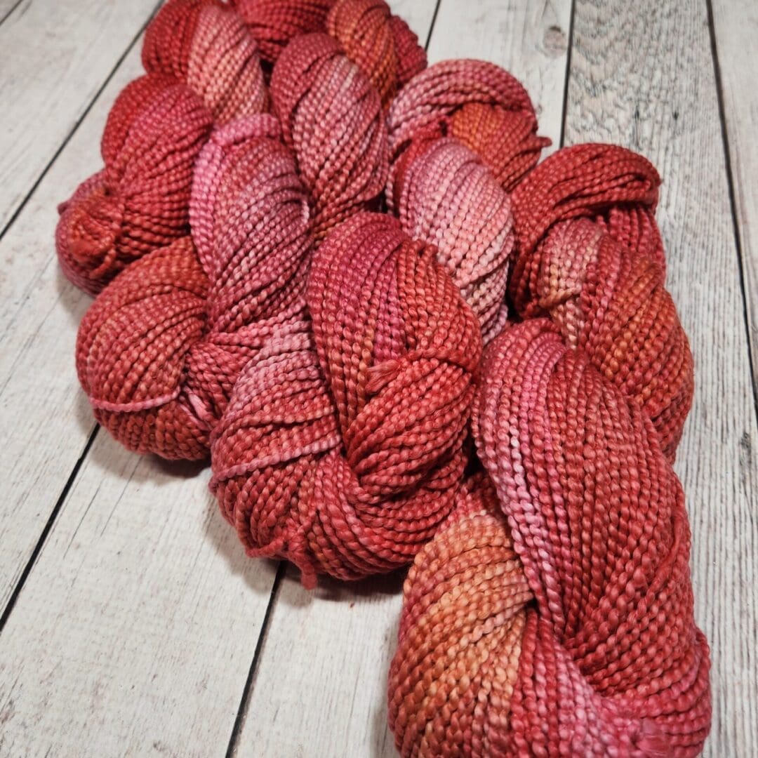 Skeins of red and orange yarn on a wooden table.