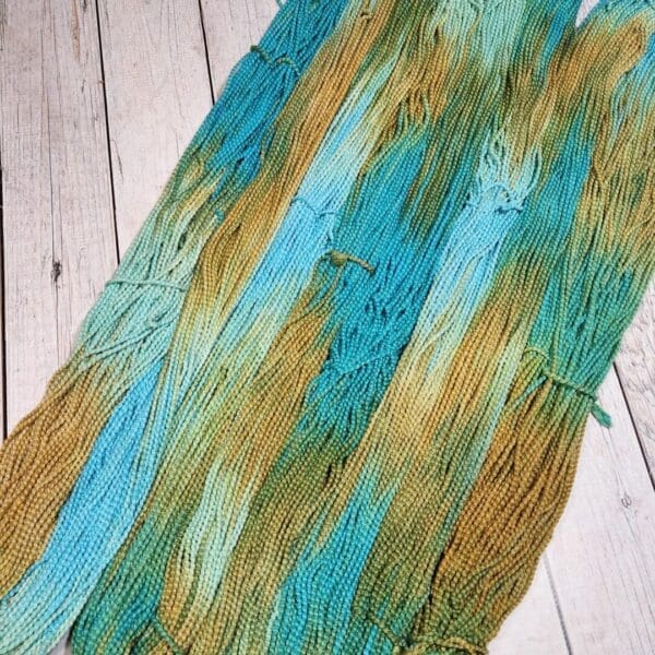 A skein of blue and green yarn on a wooden floor.