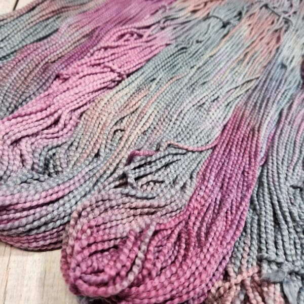 Purple and grey skeins of yarn on a wooden table.