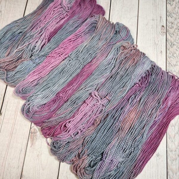 Skeins of purple and grey yarn on a wooden floor.