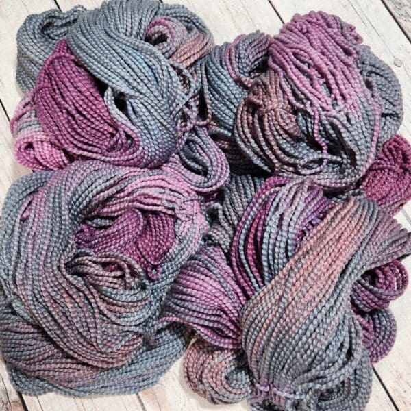 Skeins of grey and purple yarn on a wooden floor.