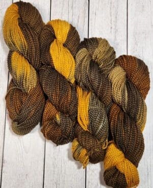 Four skeins of brown and yellow yarn on a wooden surface.