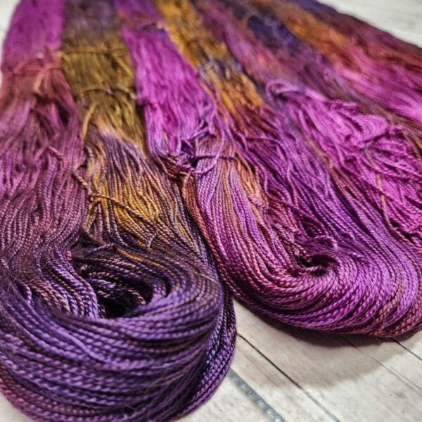 Purple and orange dyed skeins on a wooden table.