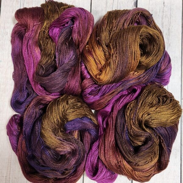 Four skeins of purple and brown yarn on a wooden surface.