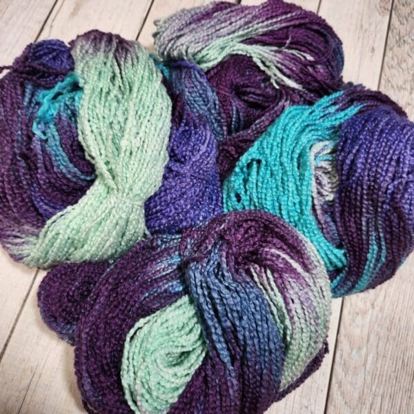 Skeins of purple and blue yarn on a wooden floor.