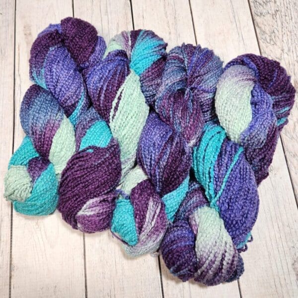 Four skeins of purple and blue yarn on a wooden floor.