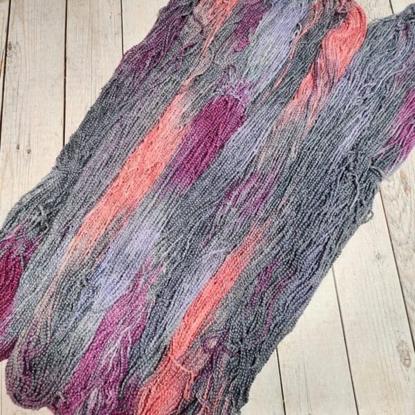 A skein of grey and pink yarn on a wooden floor.
