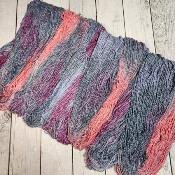 A skein of grey, pink and purple yarn on a wooden floor.