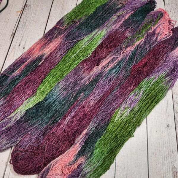 Two skeins of purple and green yarn on a wooden floor.