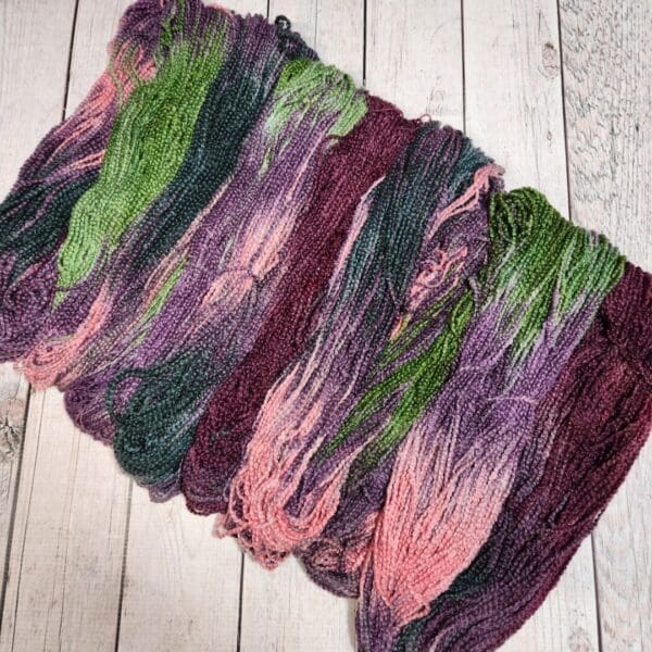 A skein of purple and green yarn on a wooden floor.