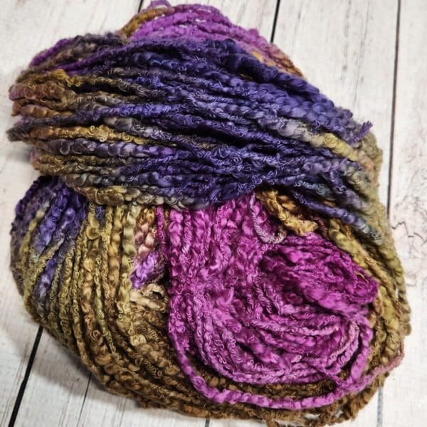 A skein of purple and green yarn on a wooden table.