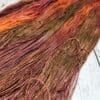 A skein of orange and brown yarn on a wooden surface.