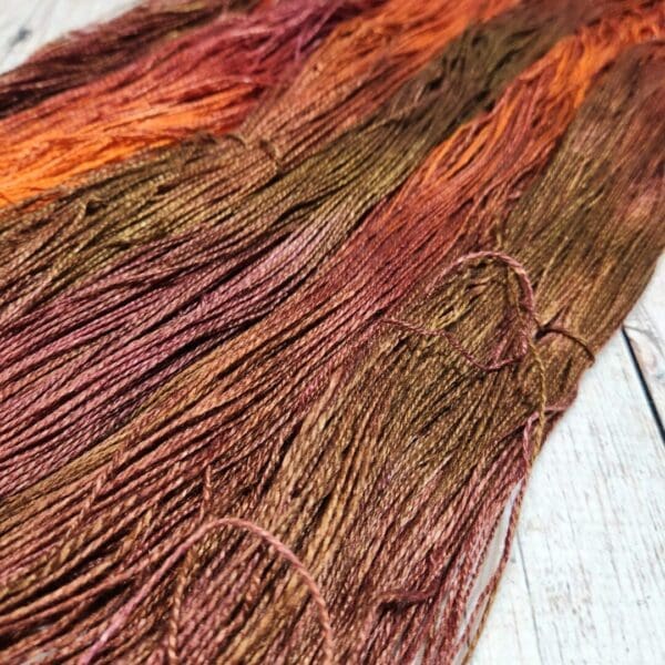 A skein of orange and brown yarn on a wooden surface.