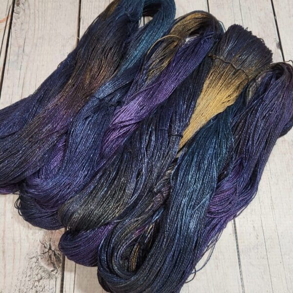 Three skeins of purple, blue and black yarn on a wooden table.