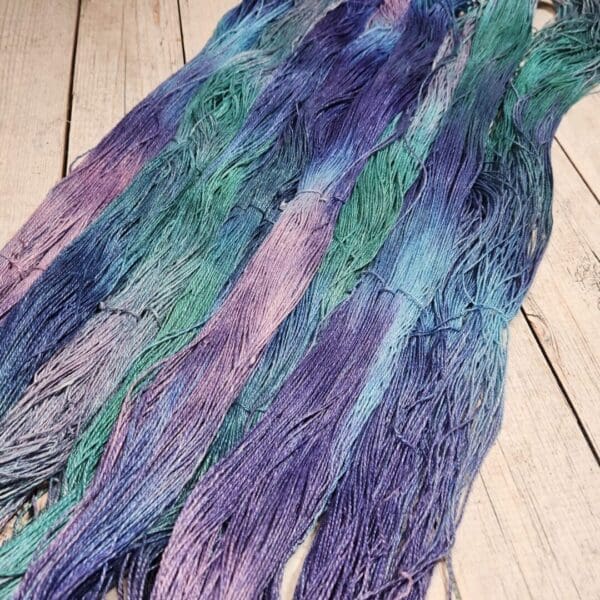 A skein of purple, blue and green yarn on a wooden floor.
