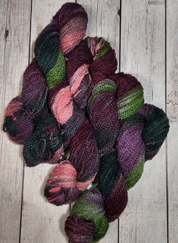 Purple and green yarn on a wooden floor.