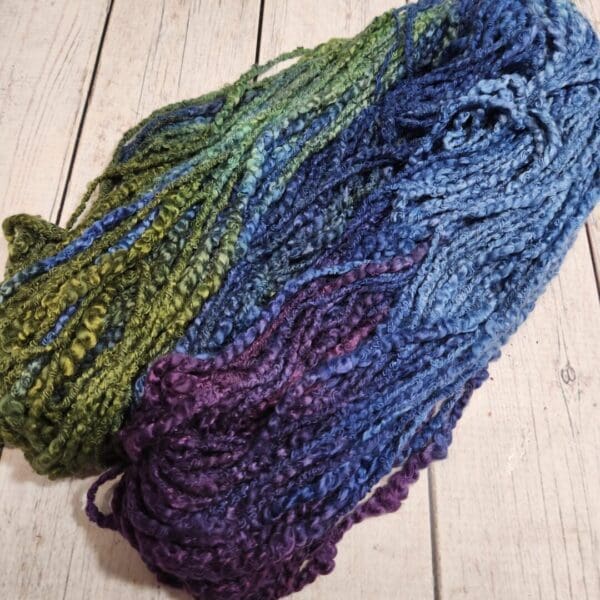 A skein of blue and green yarn on a wooden floor.