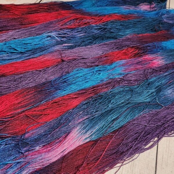 A blue, red, and purple yarn laying on a wooden floor.