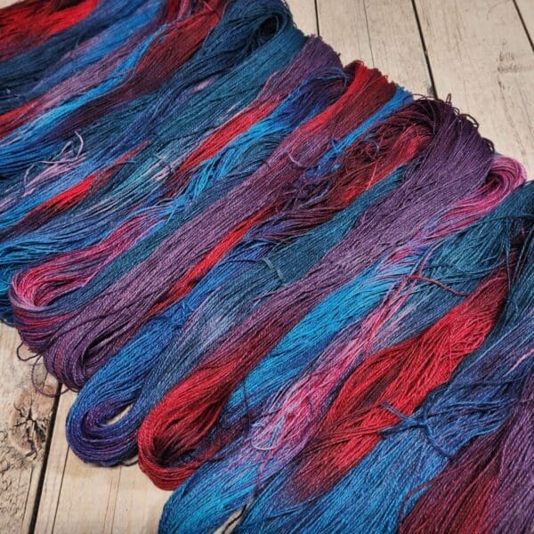 Skeins of blue, red and purple yarn on a wooden floor.