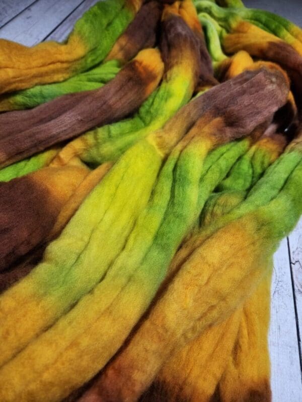 A pile of brown, yellow, and green roving on a wooden floor.