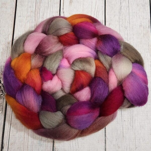 A skein of Evita - 100g Hand-Dyed Luxury Combed Top Fiber on a wooden table.